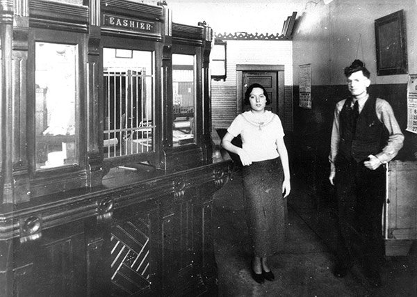 Two bank employees standing beside the cashier window of the old First State Bank