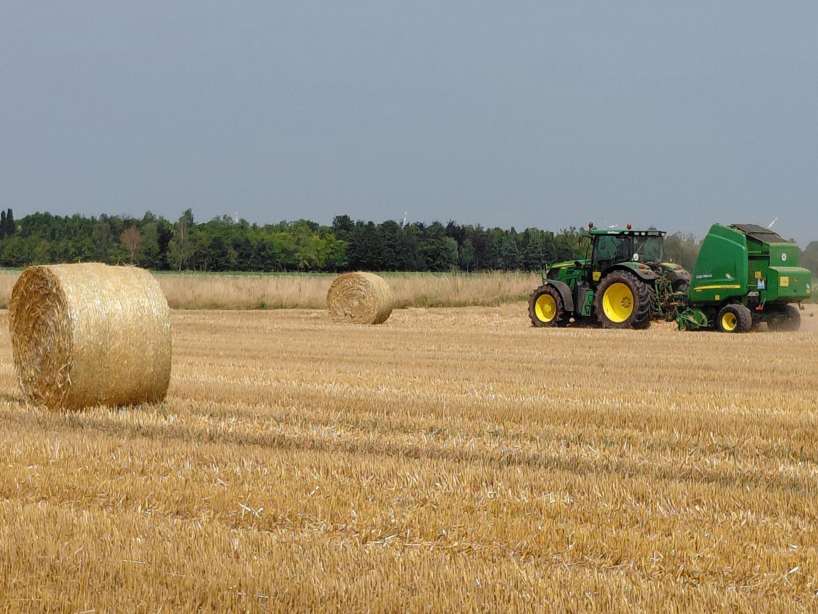 Round hay bales and a tractor in a harvested field